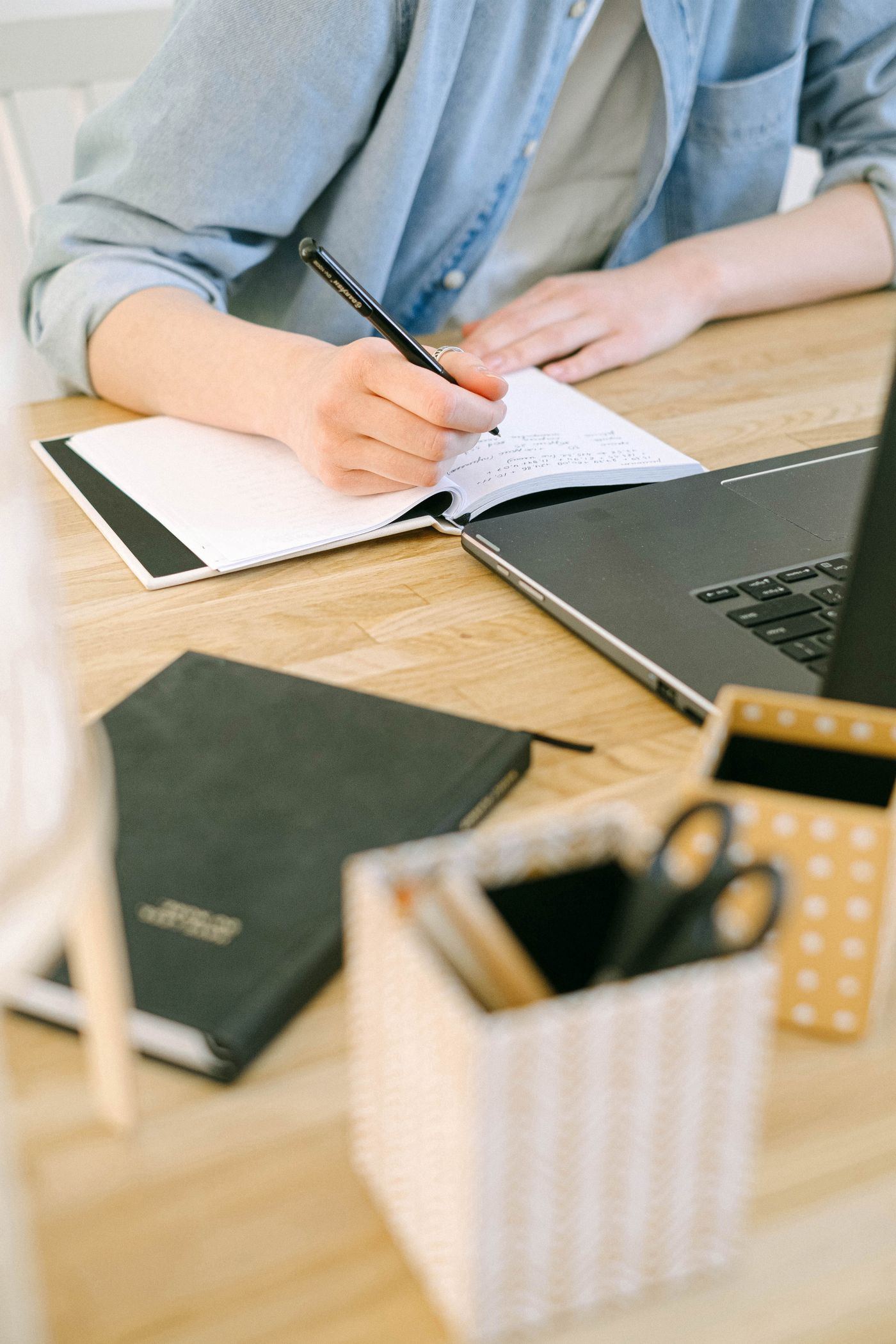 Person writing notes beside a laptop in a home workspace