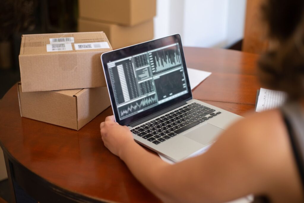 A small business owner looking at a laptop on a table stacked with cardboard boxes