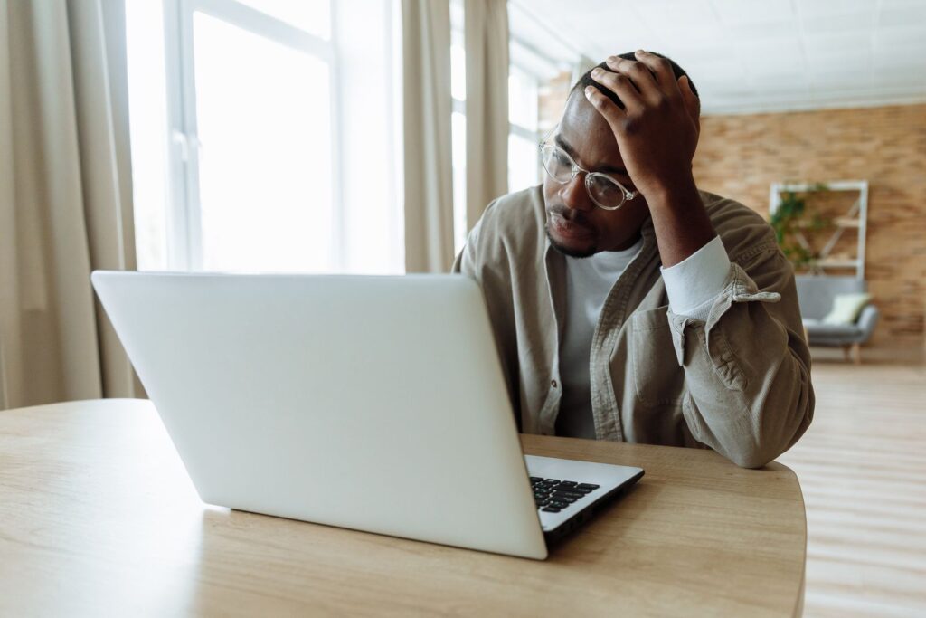 A man with his hand on his head, looking at his laptop