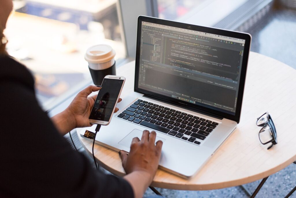 A person holding a phone beside an open laptop on a round table