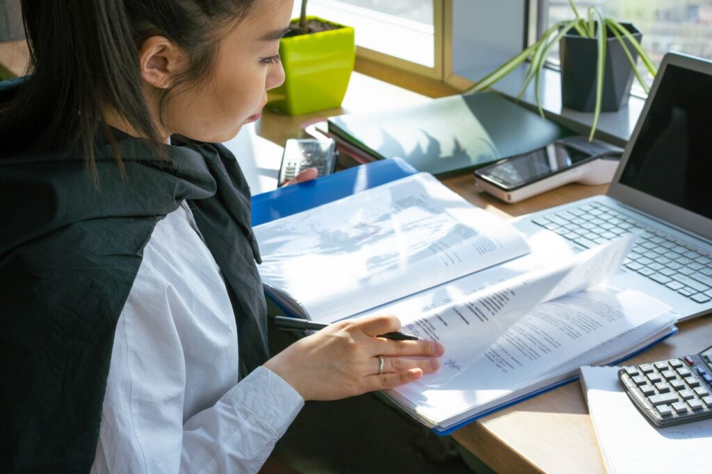 A woman reviewing documents in a folder at her desk beside a laptop